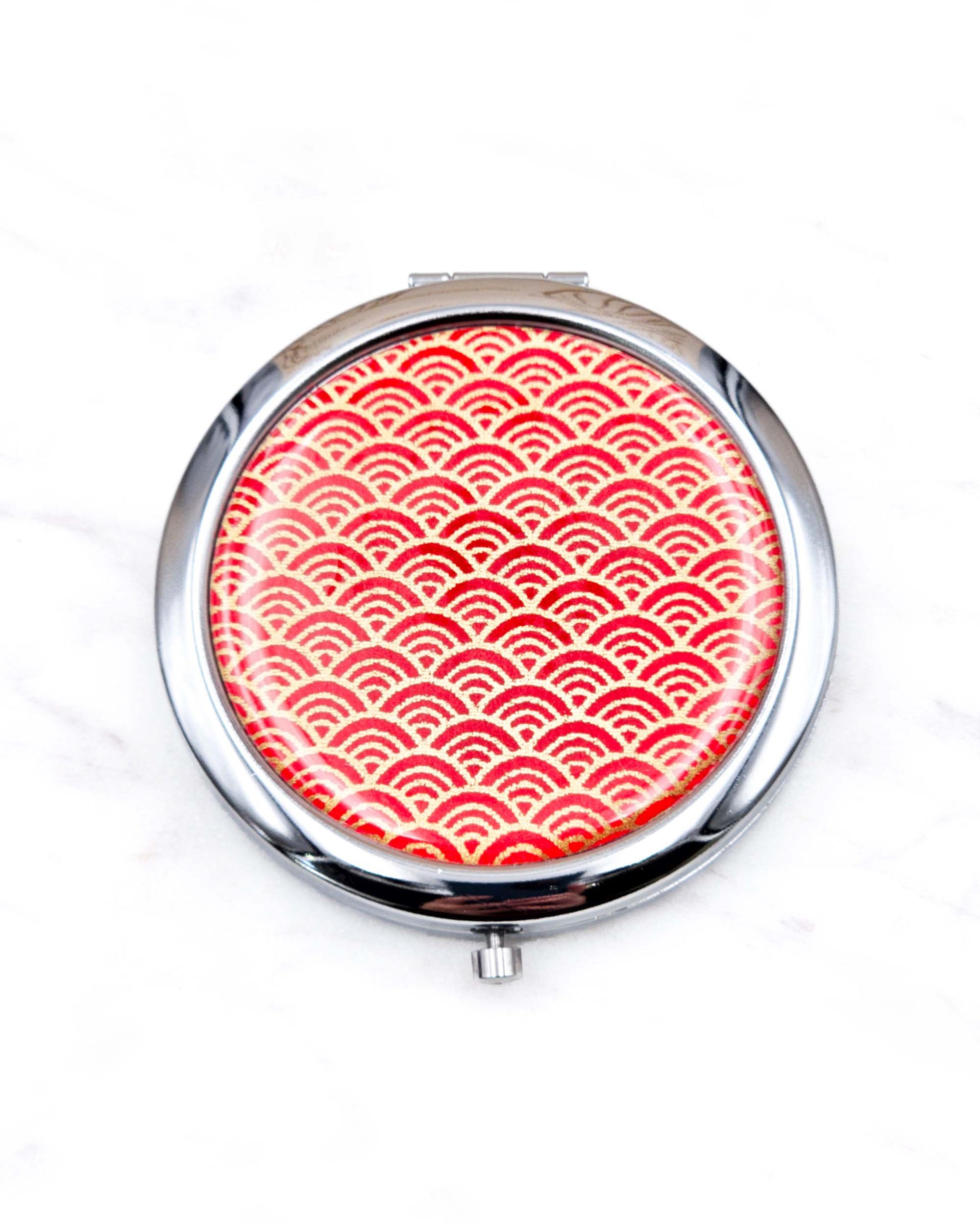 Round silver metal compact mirror featuring a small traditional red and metallic gold seigaiha (wave crests) pattern.