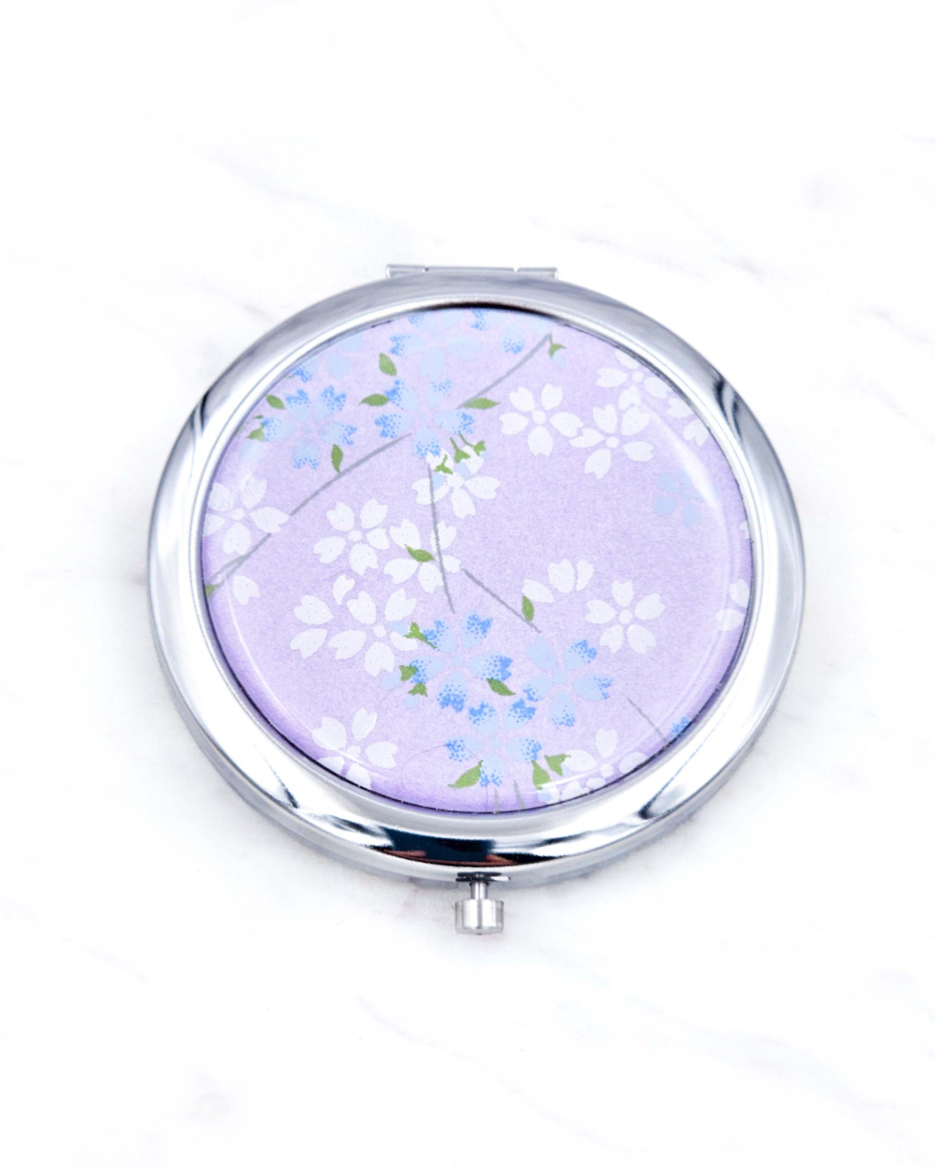 Silver metal compact mirror featuring white and blue cherry blossoms on a pearlescent purple background.