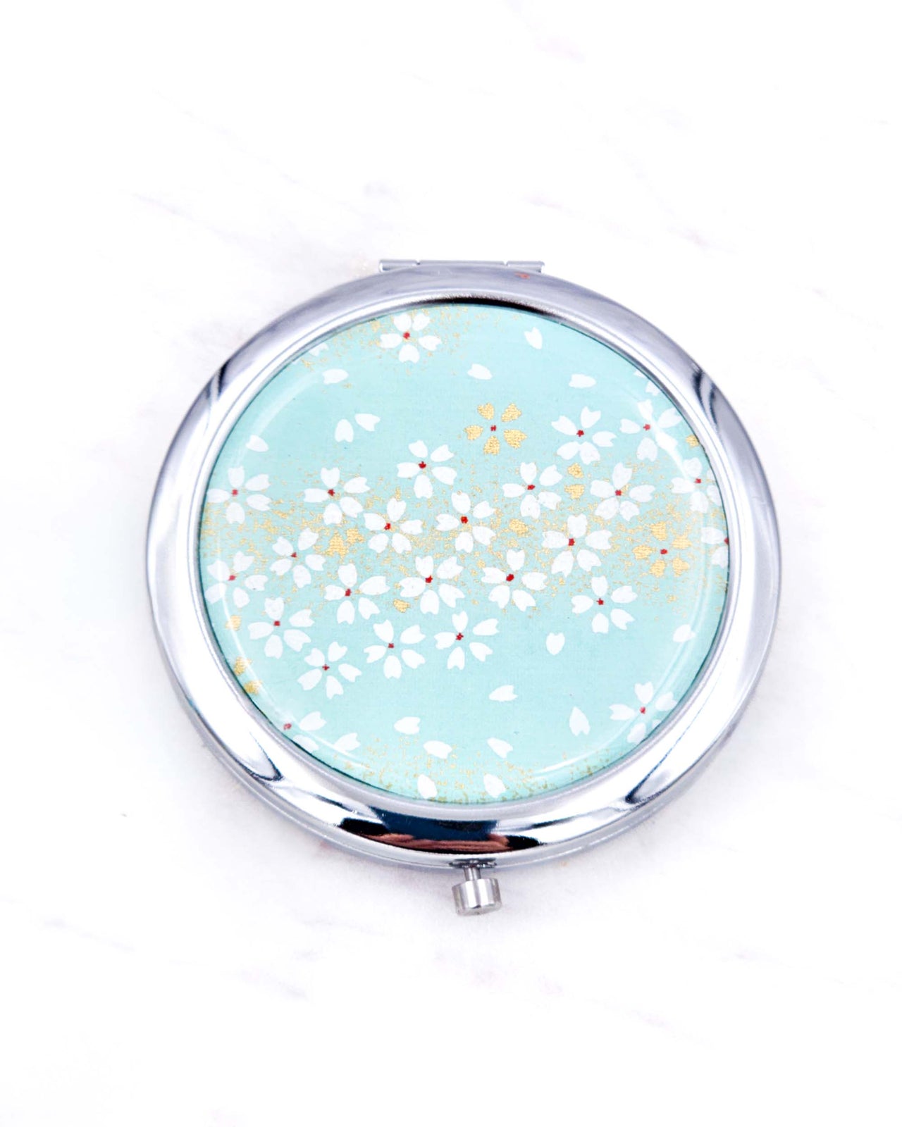Silver metal compact mirror featuring white cherry blossoms on a turquoise background with metallic gold accents.