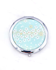 Silver metal compact mirror featuring white cherry blossoms on a turquoise background with metallic gold accents.