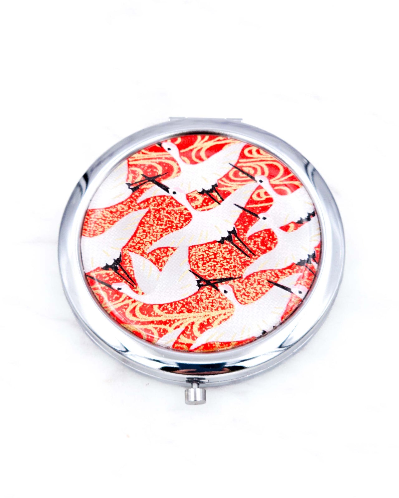 Silver metal compact mirror featuring flying white cranes on a red background with metallic gold accents