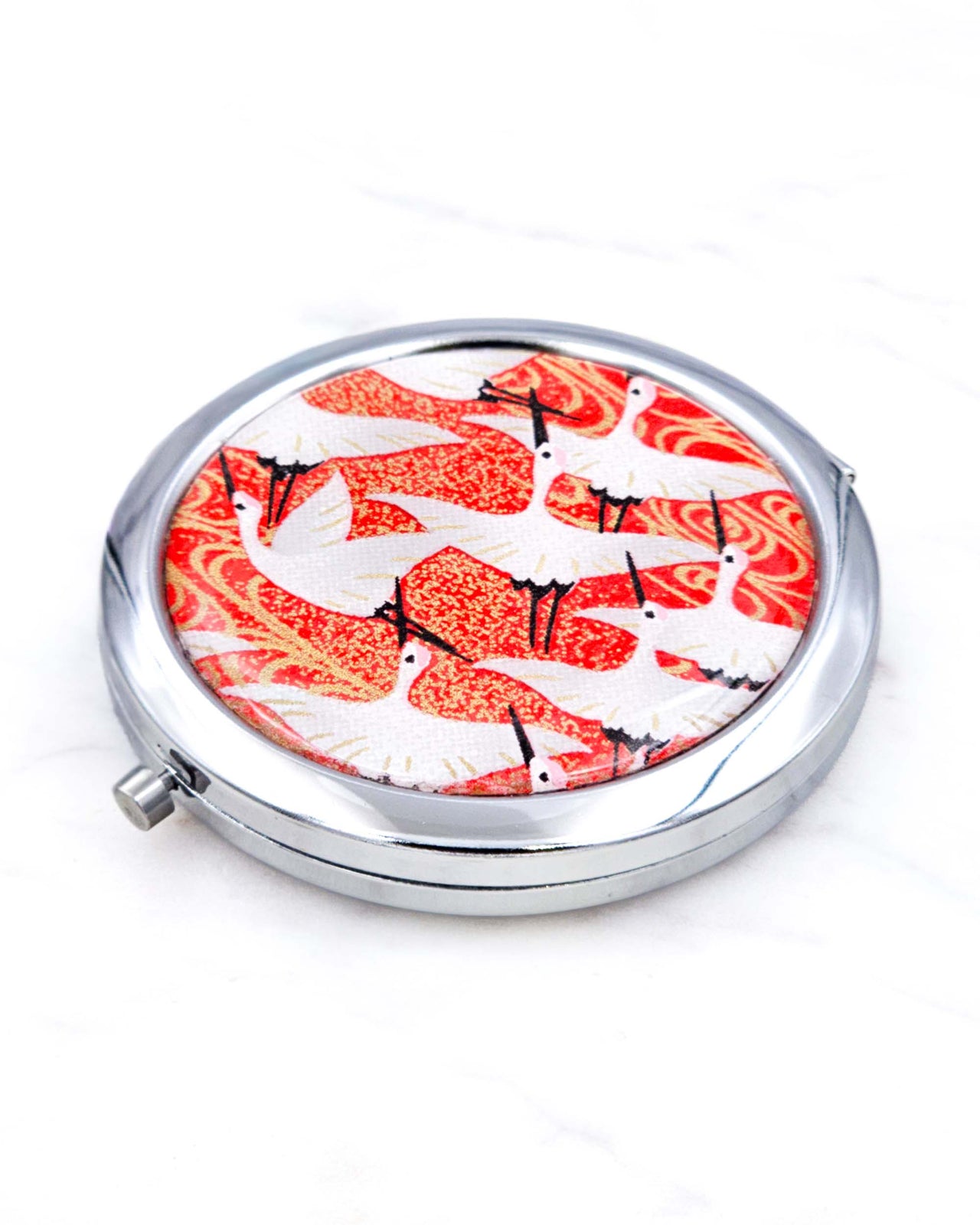 Silver metal compact mirror featuring flying white cranes on a red background with metallic gold accents