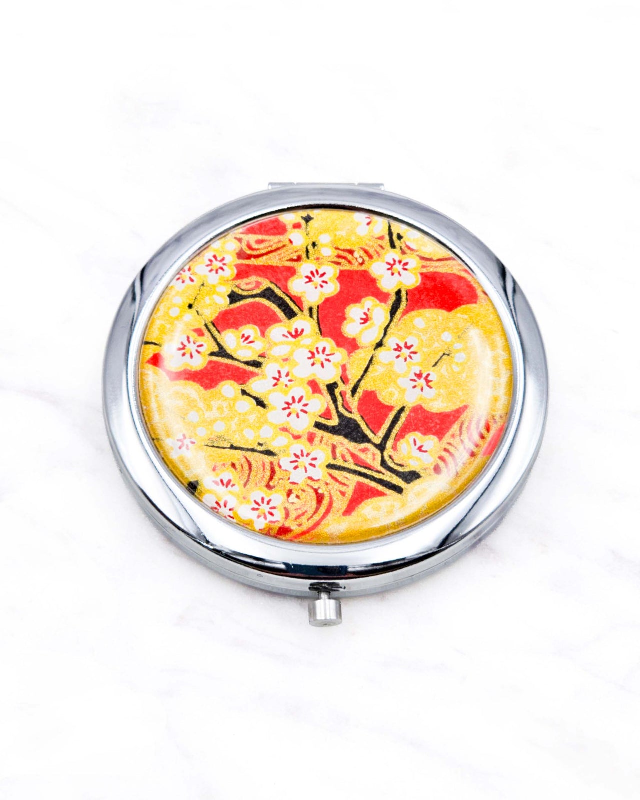 Round silver metal compact mirror featuring white plum blossom branches on a red and gold background with metallic gold accents.