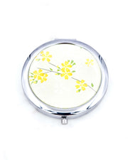 Silver metal compact mirror featuring yellow cherry blossoms on pearlescent yellow background.