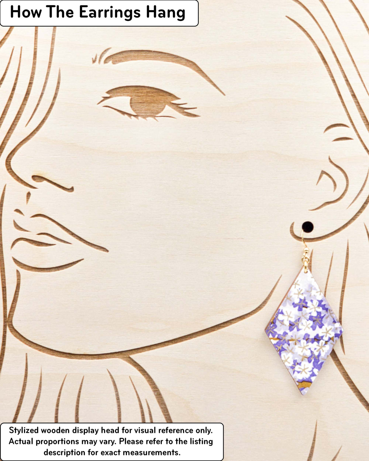 Large wooden diamond shaped earrings featuring purple and white cherry blossoms with metallic gold details, displayed on a stylized wooden head to demonstrate how the earring hangs when worn. Display is not to scale.