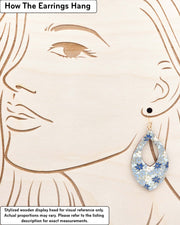 Large wooden hollow pointed teardrop shaped earrings featuring small blue and white momiji (maple leaves) on a light blue background with metallic gold details, displayed on a stylized wooden head to demonstrate how the earring hangs when worn. Display is not to scale.