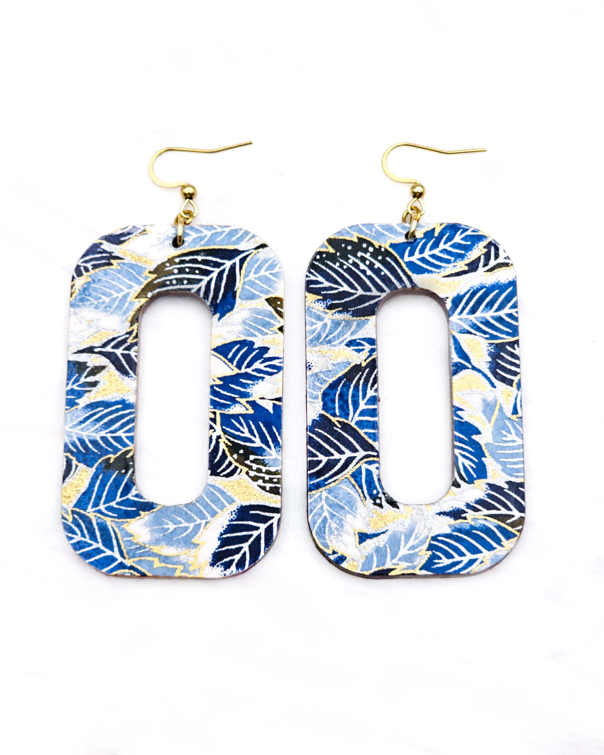 Large wooden hollow rounded rectangular earrings featuring blue, black, and white leaves on a metallic gold background