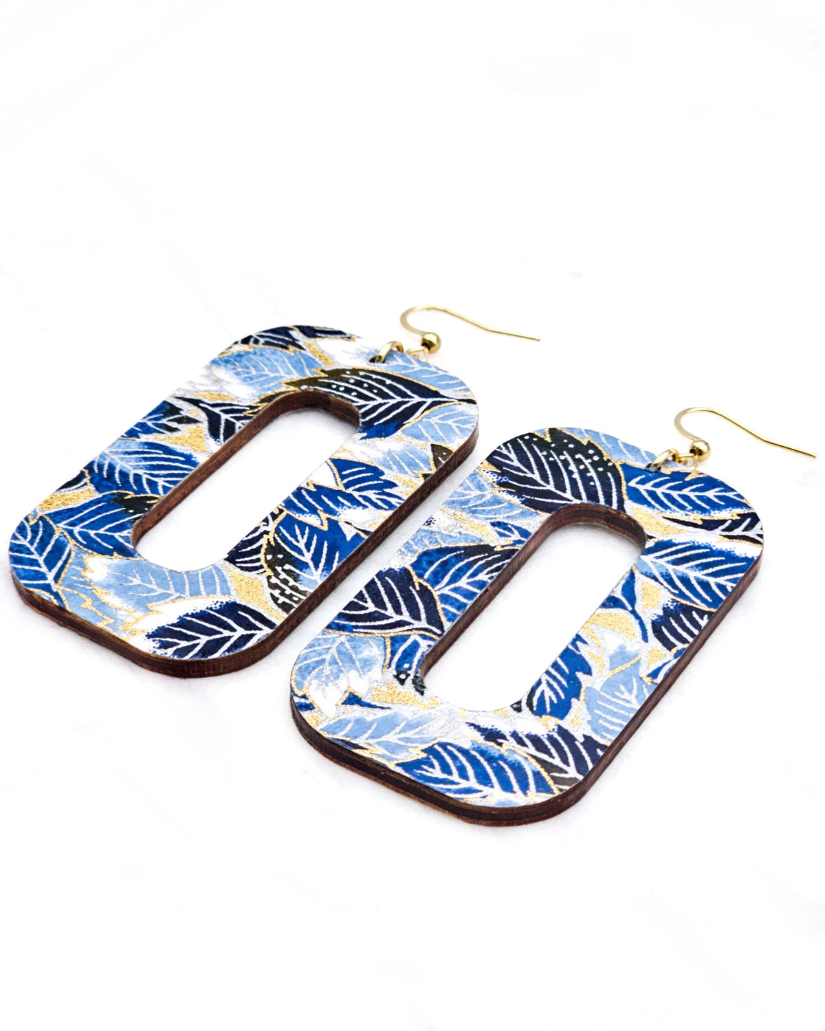 Large wooden hollow rounded rectangular earrings featuring blue, black, and white leaves on a metallic gold background
