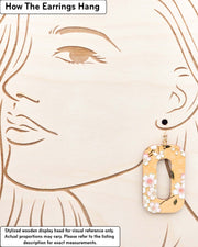Large wooden hollow rounded rectangular earrings featuring pink cherry blossoms on an orange background with metallic gold details, displayed on a stylized wooden head to demonstrate how the earring hangs when worn. Display is not to scale.