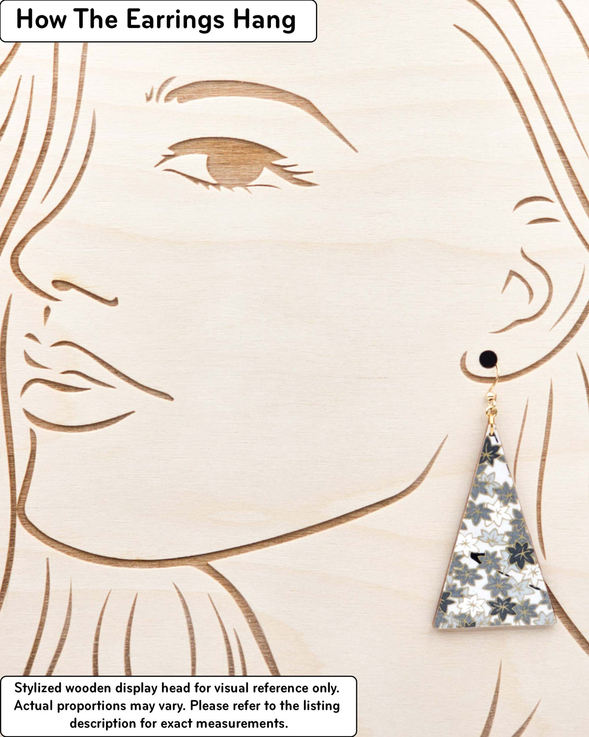 Large wooden long triangle shaped earrings featuring small gray and white momiji (maple leaves) on a light gray background with metallic gold details, displayed on a stylized wooden head to demonstrate how the earring hangs when worn. Display is not to scale.