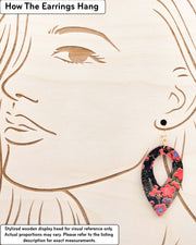 Large wooden hollow reverse teardrop earrings featuring red plum blossoms with a little bit of blue on a black background with metallic gold details, displayed on a stylized wooden head to demonstrate how the earring hangs when worn. Display is not to scale.