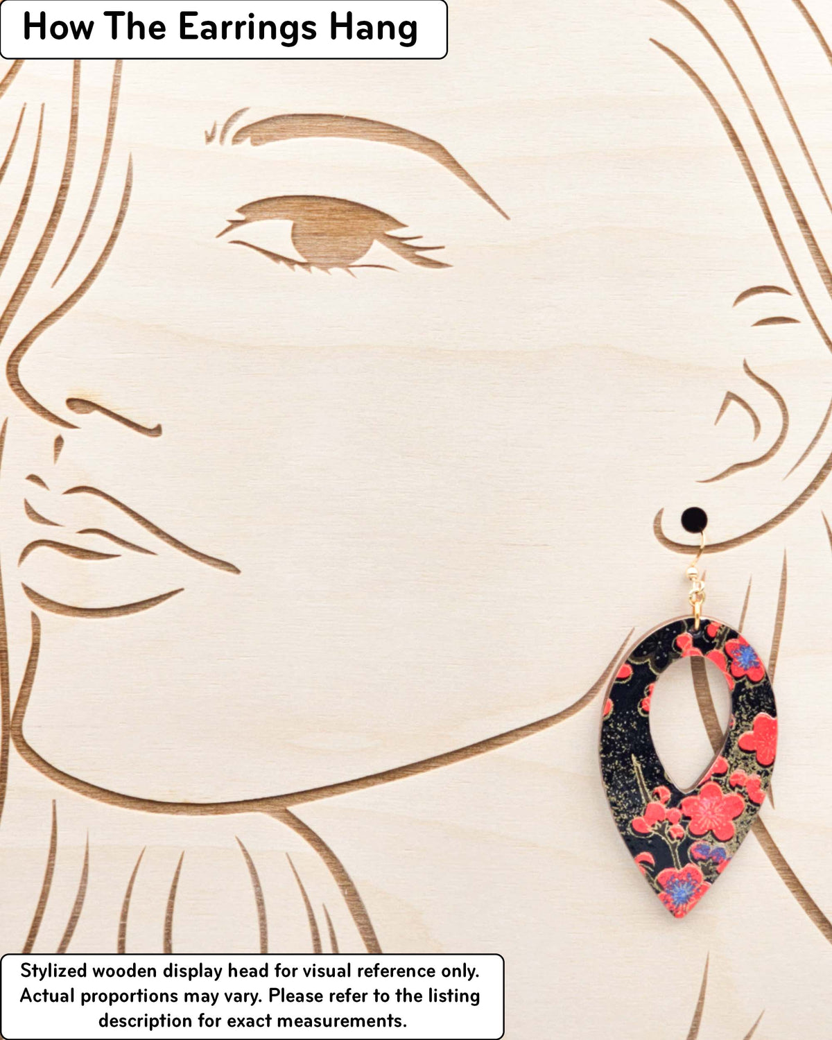 Large wooden hollow reverse teardrop earrings featuring red plum blossoms with a little bit of blue on a black background with metallic gold details, displayed on a stylized wooden head to demonstrate how the earring hangs when worn. Display is not to scale.