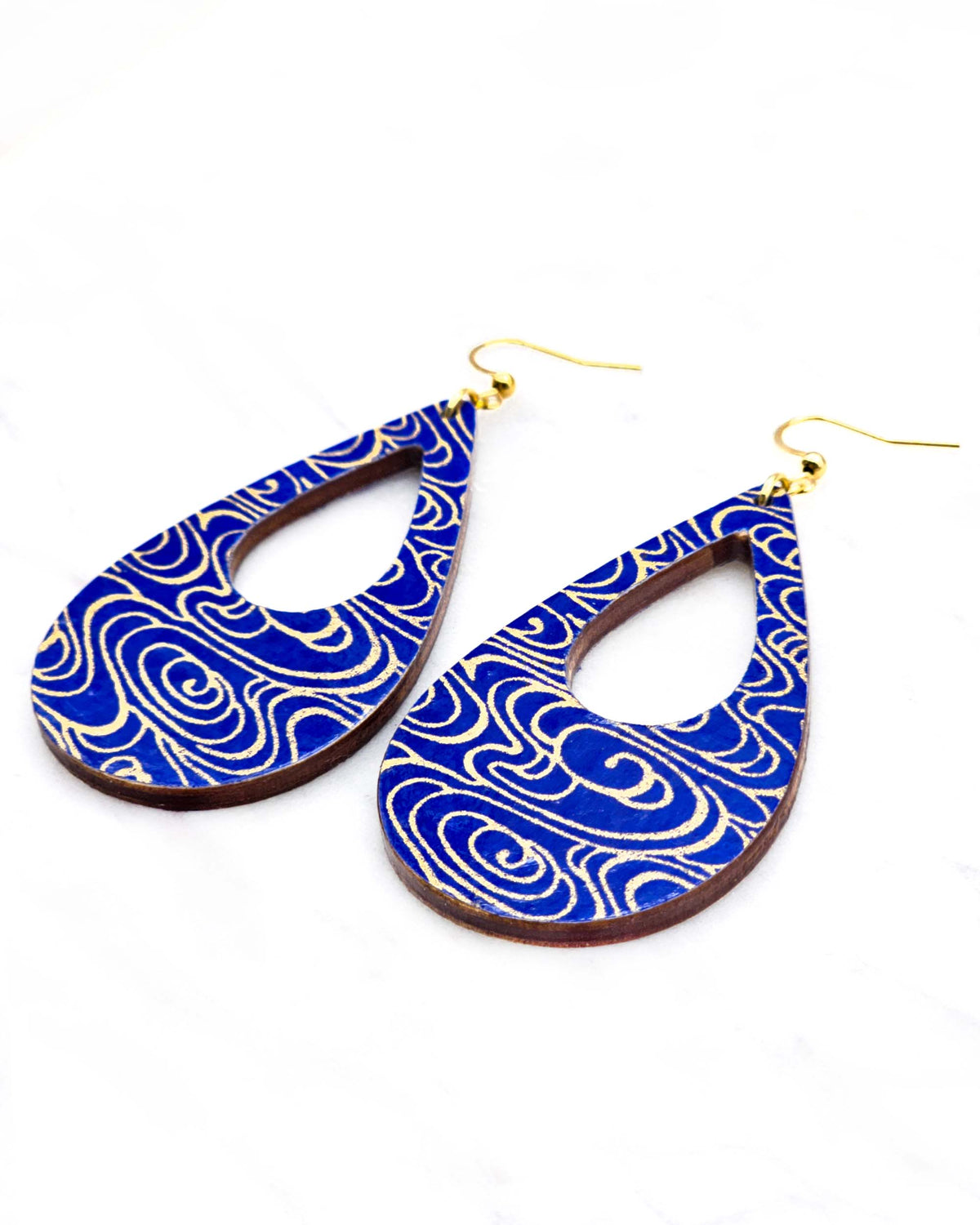 Large wooden hollow teardrop earrings featuring metallic gold water ripples on a dark blue background.