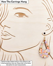 Large wooden hollow teardrop earrings featuring orange, brown, and light purple lotuses on a brown background with metallic gold details, displayed on a stylized wooden head to demonstrate how the earring hangs when worn. Display is not to scale.
