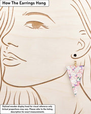Large wooden long triangle shaped earrings featuring pink and white cherry blossoms on a pearlescent light purple background with metallic gold details, displayed on a stylized wooden head to demonstrate how the earring hangs when worn. Display is not to scale.