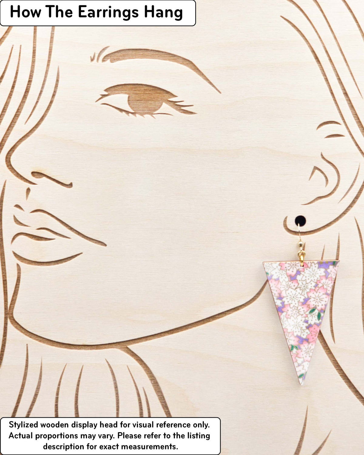 Large wooden long triangle shaped earrings featuring pink and white cherry blossoms on a pearlescent light purple background with metallic gold details, displayed on a stylized wooden head to demonstrate how the earring hangs when worn. Display is not to scale.