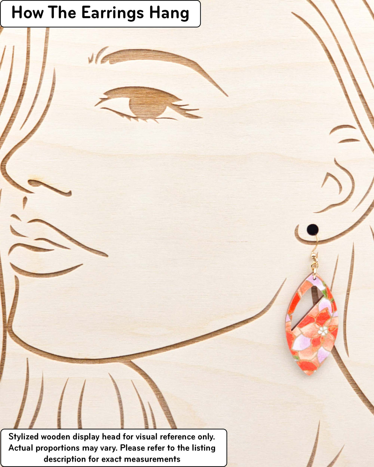 Medium wooden cutout pointed oval shaped earrings featuring orange and purple lotuses on a green background with metallic gold details, displayed on a stylized wooden head to demonstrate how the earring hangs when worn. Display is not to scale.