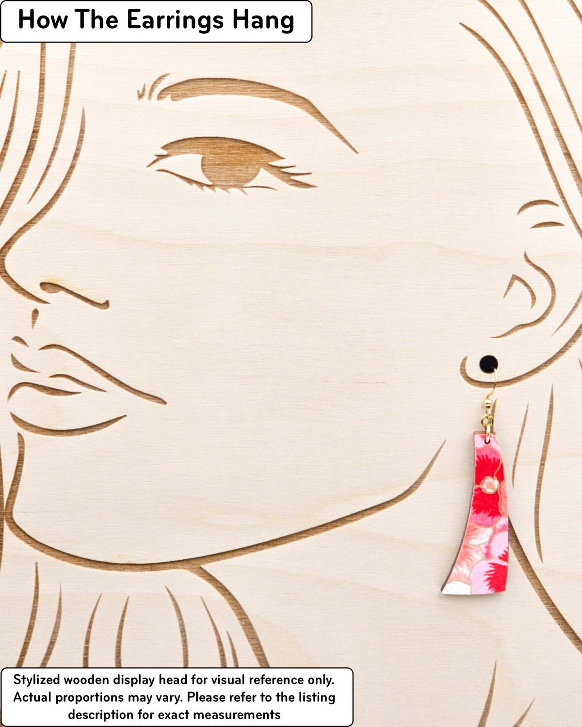 Medium wooden curved bar shaped earrings featuring pink and white pansies with with metallic gold details, displayed on a stylized wooden head to demonstrate how the earring hangs when worn. Display is not to scale.
