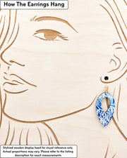 Medium wooden hollow reverse teardrop shaped earrings featuring blue chrysanthemums on a dark blue background with metallic gold details, displayed on a stylized wooden head to demonstrate how the earring hangs when worn. Display is not to scale.