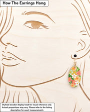 Medium wooden oval shaped earrings featuring assorted green, white, pink, and orange flowers on a green background with metallic gold details, displayed on a stylized wooden head to demonstrate how the earring hangs when worn. Display is not to scale.