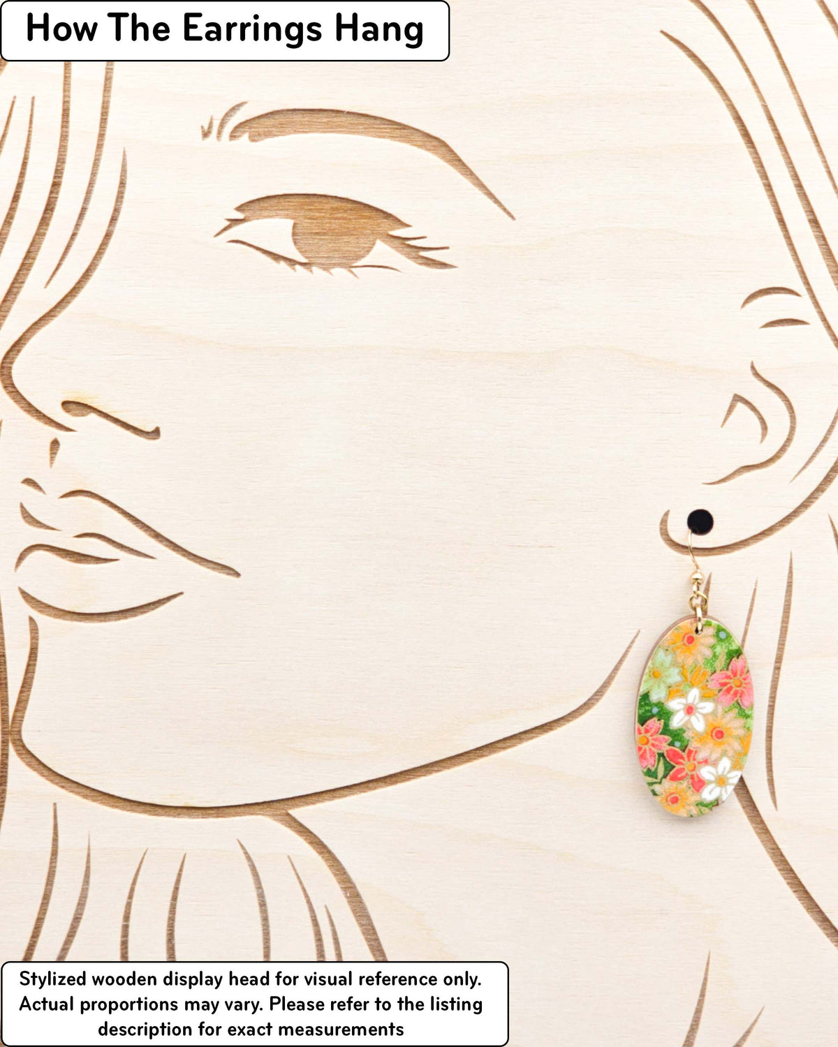 Medium wooden oval shaped earrings featuring assorted green, white, pink, and orange flowers on a green background with metallic gold details, displayed on a stylized wooden head to demonstrate how the earring hangs when worn. Display is not to scale.