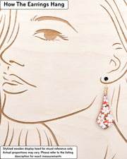 Medium wooden long anchor shaped earrings featuring white and pink cherry blossoms on a reddish orange background with metallic gold details, displayed on a stylized wooden head to demonstrate how the earring hangs when worn. Display is not to scale.