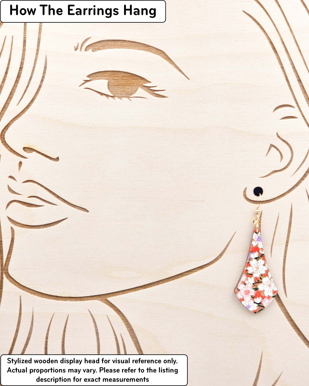 Medium wooden long anchor shaped earrings featuring white and pink cherry blossoms on a reddish orange background with metallic gold details, displayed on a stylized wooden head to demonstrate how the earring hangs when worn. Display is not to scale.