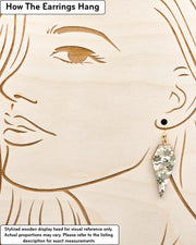 Medium wooden long diamond shaped earrings featuring small gray and white momiji (maple leaves) on a light gray background with metallic gold details, displayed on a stylized wooden head to demonstrate how the earring hangs when worn. Display is not to scale.