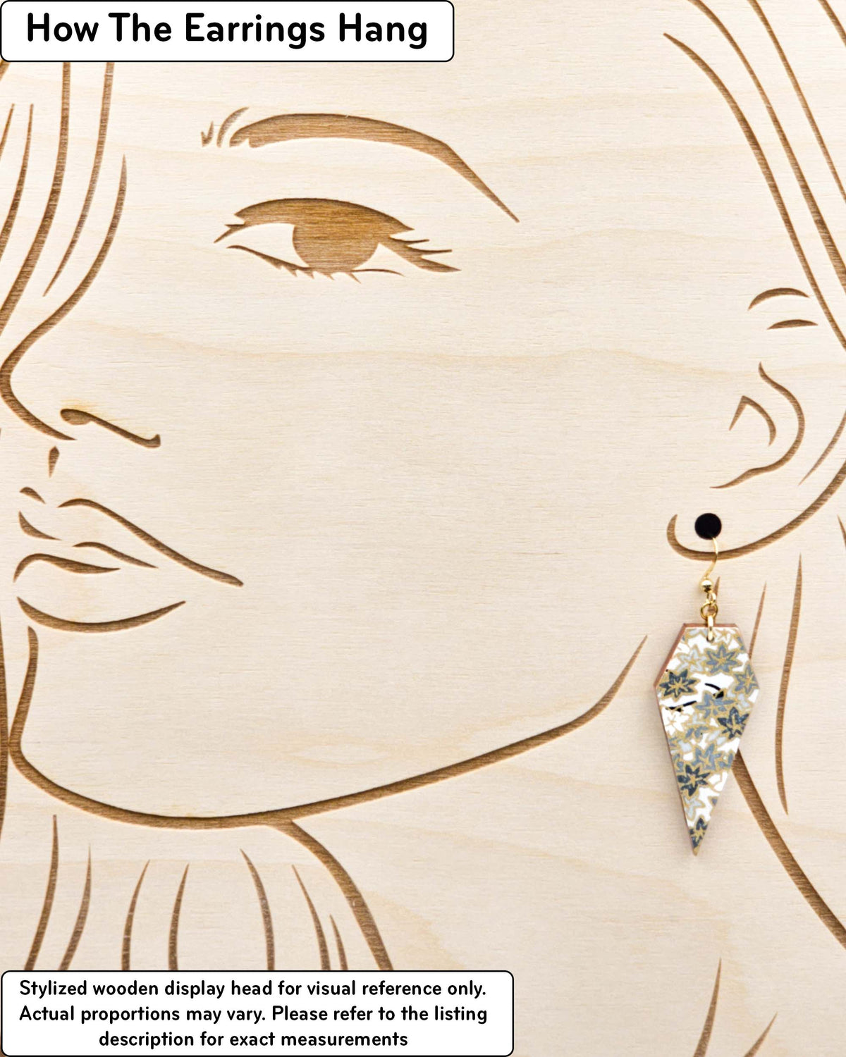 Medium wooden long diamond shaped earrings featuring small gray and white momiji (maple leaves) on a light gray background with metallic gold details, displayed on a stylized wooden head to demonstrate how the earring hangs when worn. Display is not to scale.
