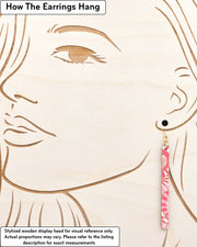 Medium wooden long thin bar shaped earrings featuring pink and white overlapping parasols with metallic gold details, displayed on a stylized wooden head to demonstrate how the earring hangs when worn. Display is not to scale.