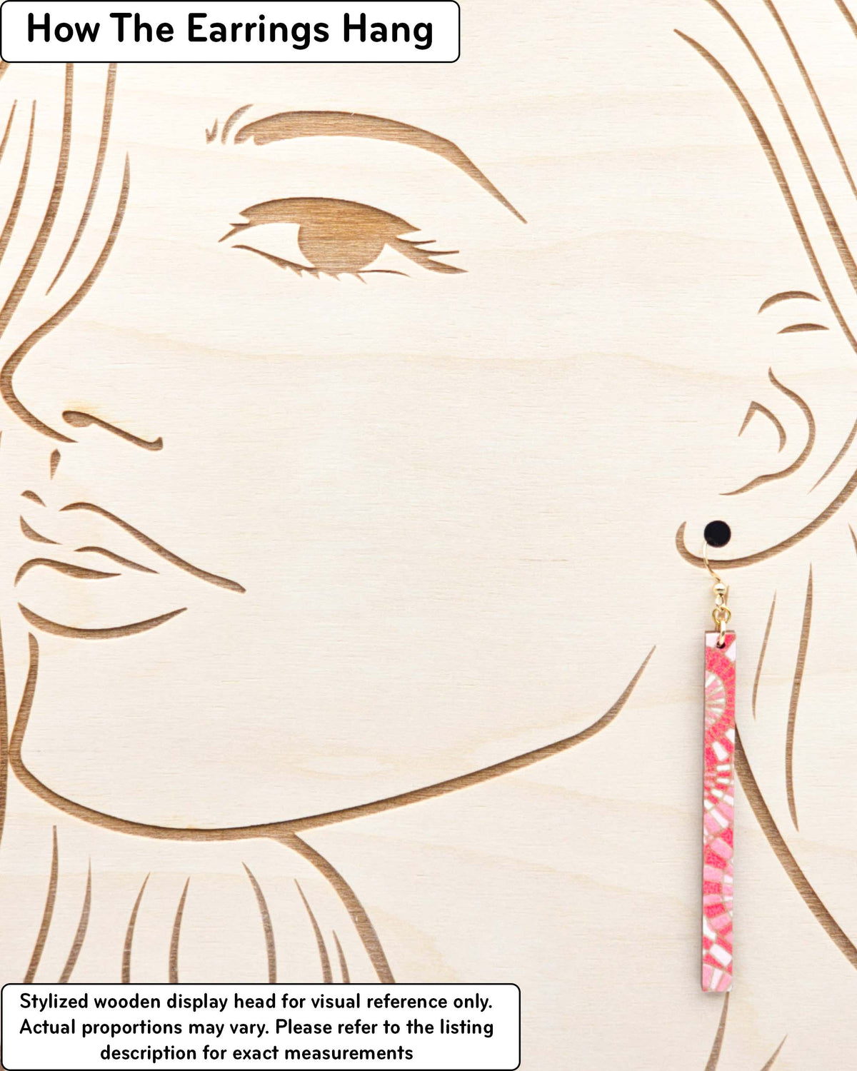 Medium wooden long thin bar shaped earrings featuring pink and white overlapping parasols with metallic gold details, displayed on a stylized wooden head to demonstrate how the earring hangs when worn. Display is not to scale.