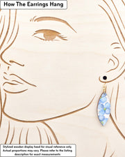 Medium wooden thin pointed oval shaped earrings featuring blue flowers on a pink background with metallic gold details, displayed on a stylized wooden head to demonstrate how the earring hangs when worn. Display is not to scale.