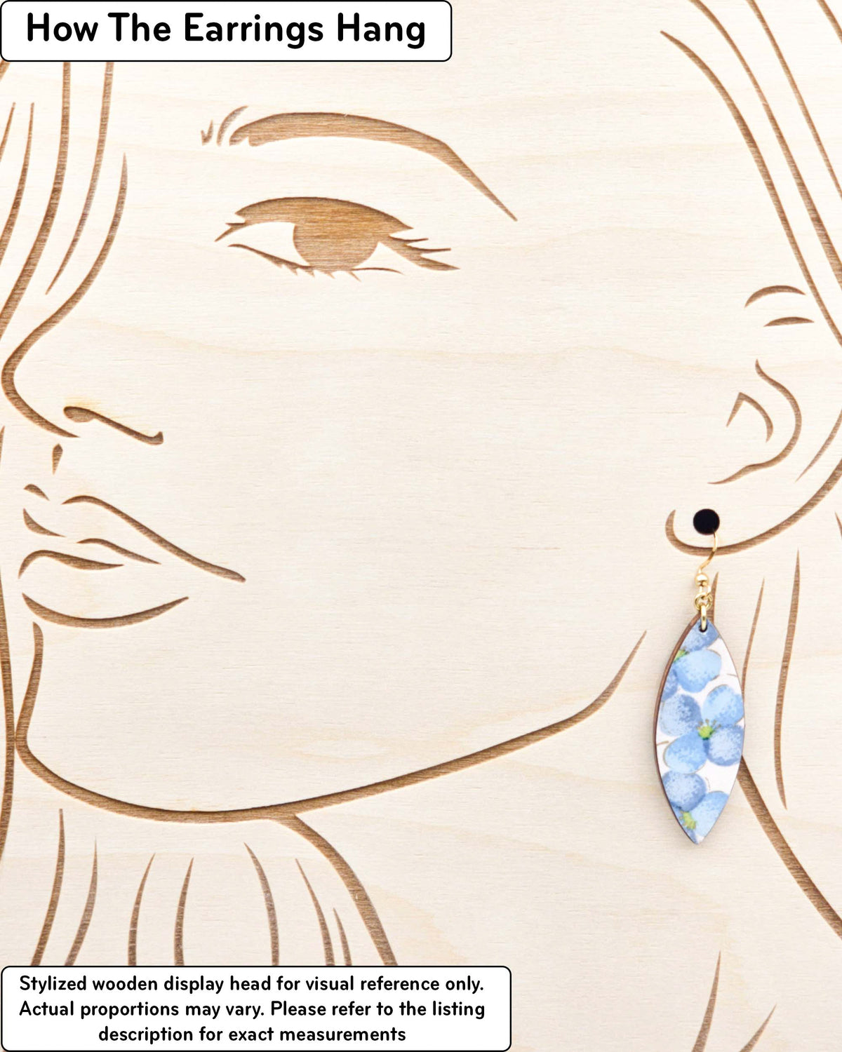 Medium wooden thin pointed oval shaped earrings featuring blue flowers on a pink background with metallic gold details, displayed on a stylized wooden head to demonstrate how the earring hangs when worn. Display is not to scale.