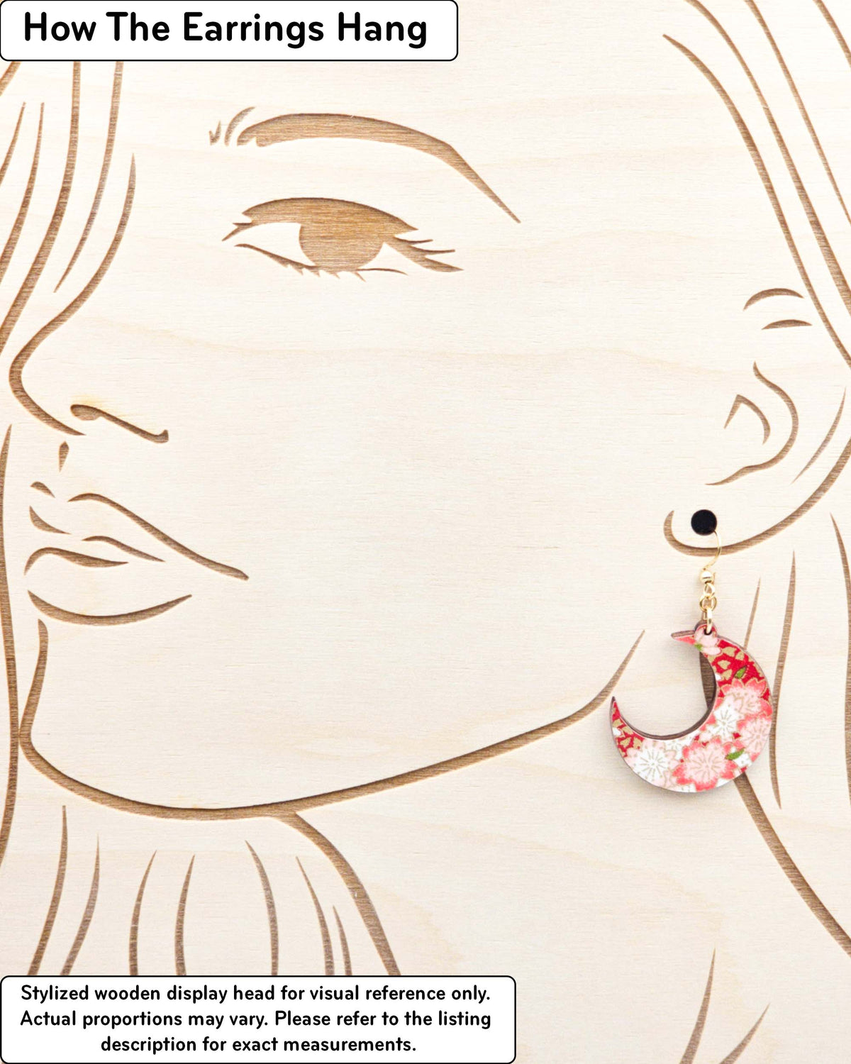 Medium wooden crescent moon shaped earrings featuring red and white cherry blossoms on a red background with metallic gold details, displayed on a stylized wooden head to demonstrate how the earring hangs when worn. Display is not to scale.