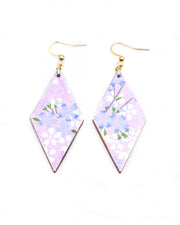 Medium wooden diamond shaped earrings featuring light blue and white cherry blossoms with green leaves and branches on a pearlescent light purple background.
