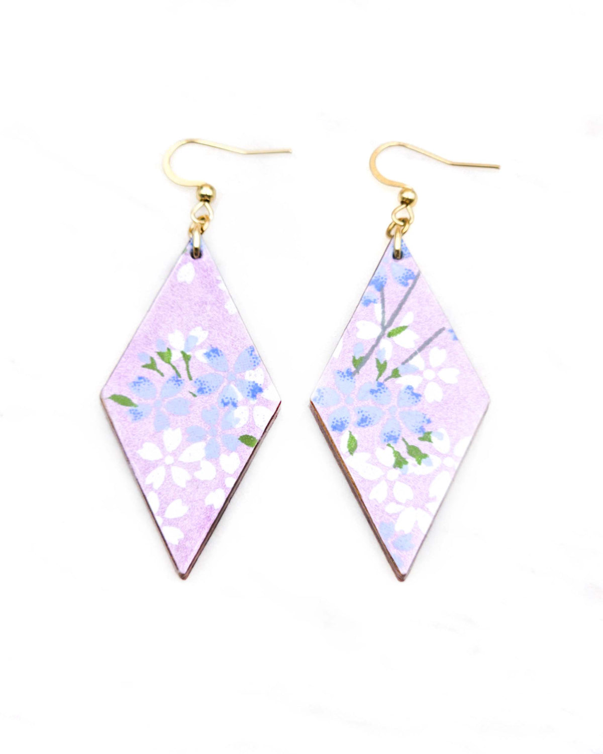 Medium wooden diamond shaped earrings featuring light blue and white cherry blossoms with green leaves and branches on a pearlescent light purple background.