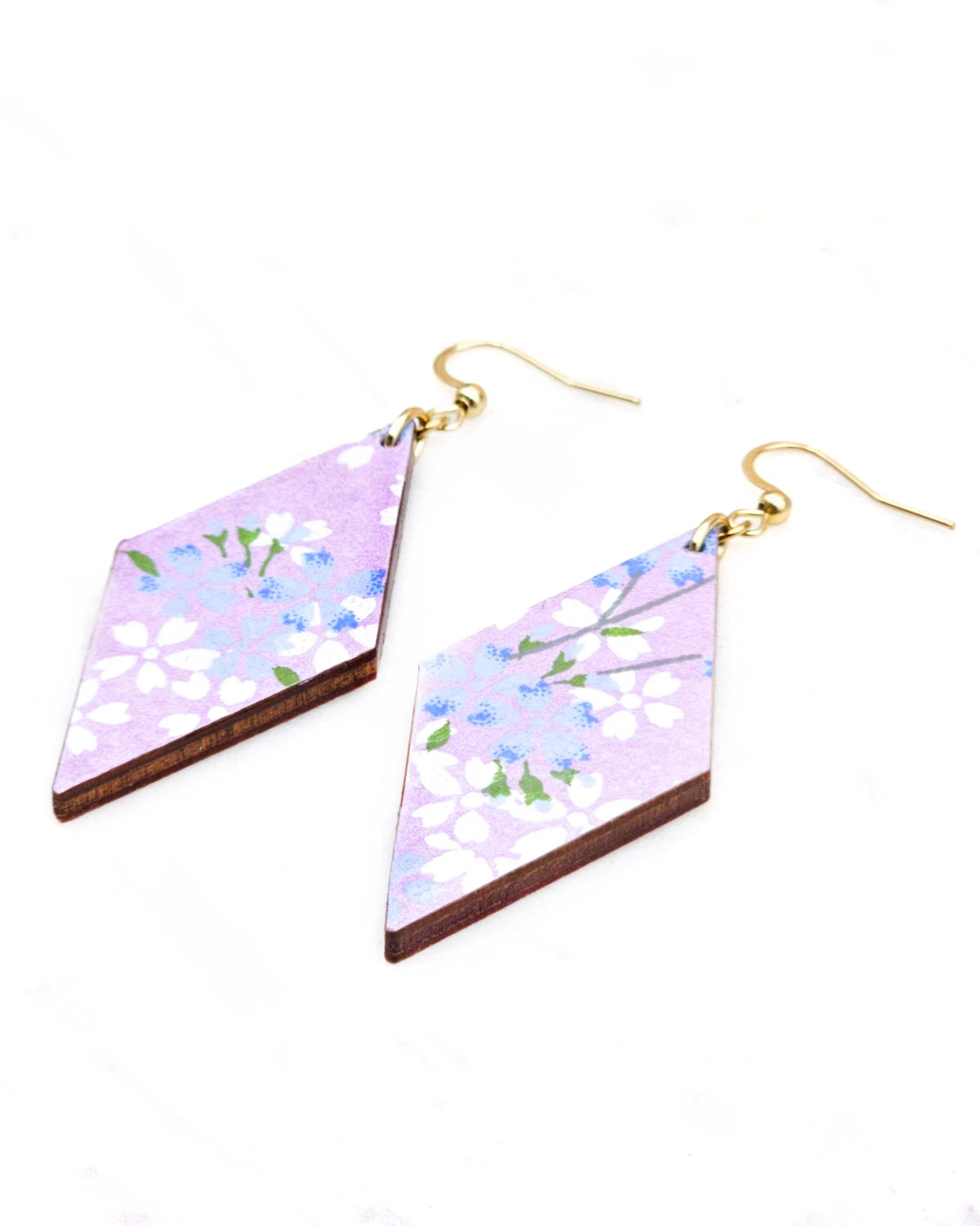 Medium wooden diamond shaped earrings featuring light blue and white cherry blossoms with green leaves and branches on a pearlescent light purple background.