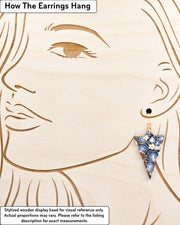 Medium wooden notched triangle shaped earrings featuring blue and gray plum blossoms with brown branches on a dark blue background with metallic gold details, displayed on a stylized wooden head to demonstrate how the earring hangs when worn. Display is not to scale.