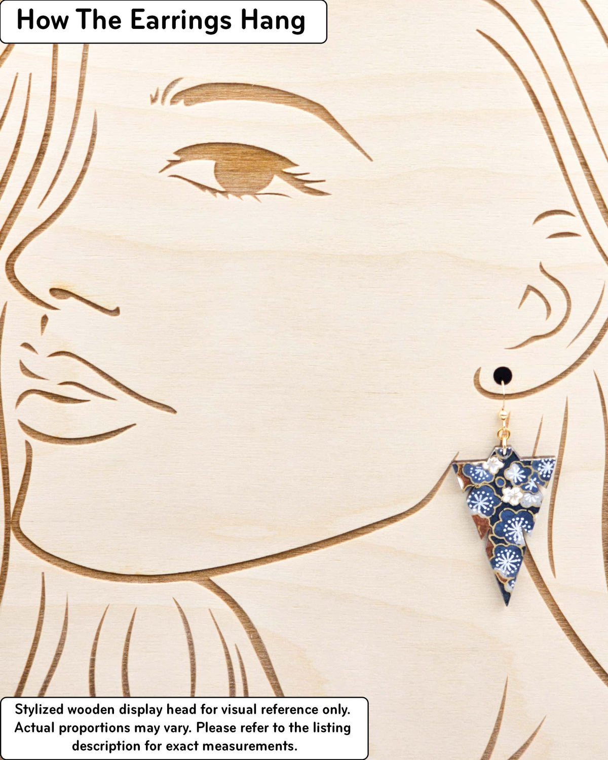 Medium wooden notched triangle shaped earrings featuring blue and gray plum blossoms with brown branches on a dark blue background with metallic gold details, displayed on a stylized wooden head to demonstrate how the earring hangs when worn. Display is not to scale.
