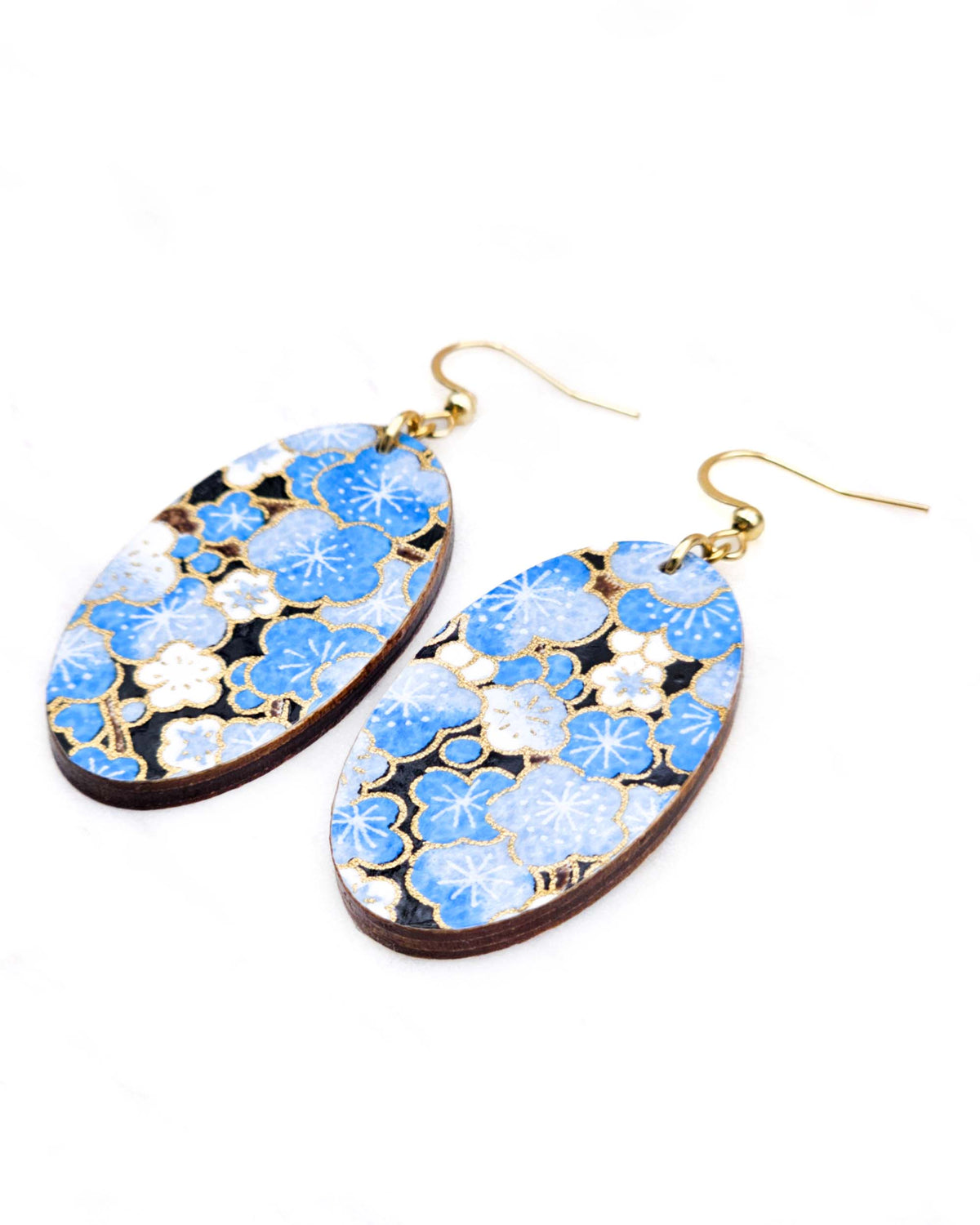 Medium wooden oval shaped earrings featuring blue plum blossoms on a black background with metallic gold details.