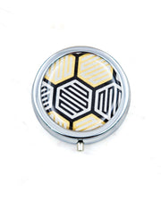 Round silver metal pill box featuring a traditional black, white, and gold kikkou pattern.