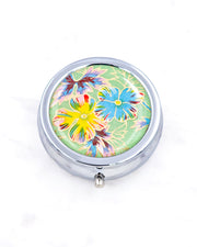 Silver metal pill box featuring blue and yellow flowers on a green background with metallic gold accents.