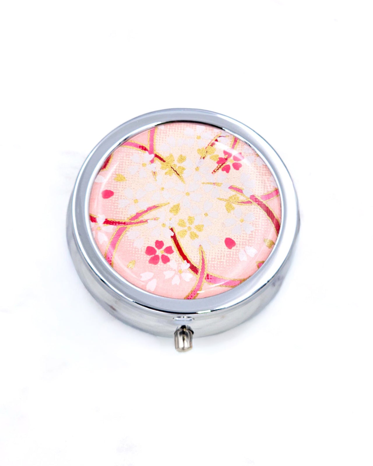 Silver metal pill box featuring white and gold cherry blossoms on a pink background with metallic gold accents.