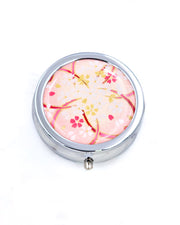 Silver metal pill box featuring white and gold cherry blossoms on a pink background with metallic gold accents.