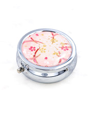 Silver metal pill box featuring white and gold cherry blossoms on a pink background with metallic gold accents.
