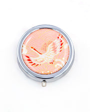 Silver metal pill box featuring a flying crane on a pink background with metallic gold accent.