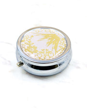 Round silver metal pill box featuring metallic gold Mt Fuji and cherry blossoms on a light pink background.