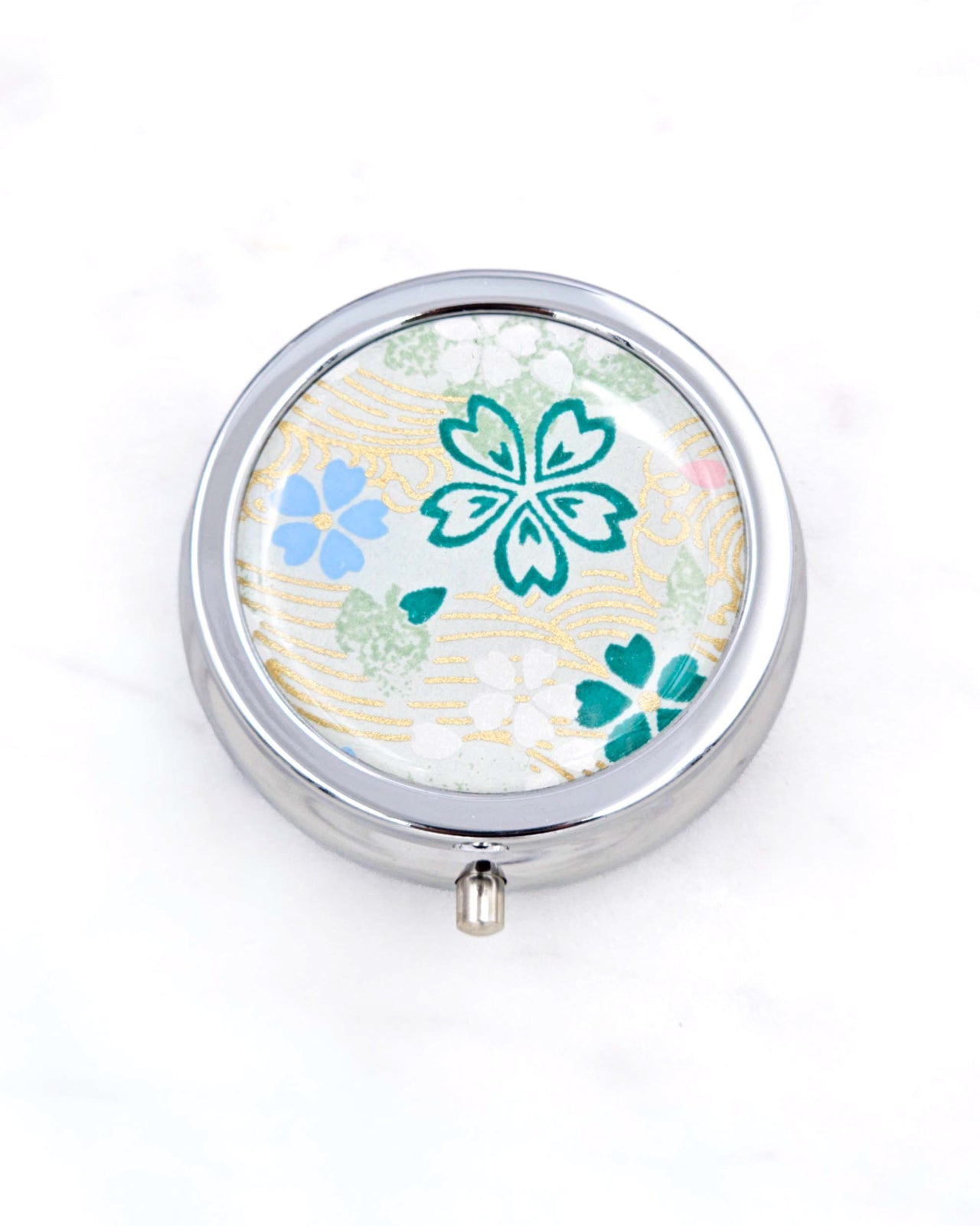 Silver metal pill box featuring green, white, and blue cherry blossoms on green background with metallic gold accents.