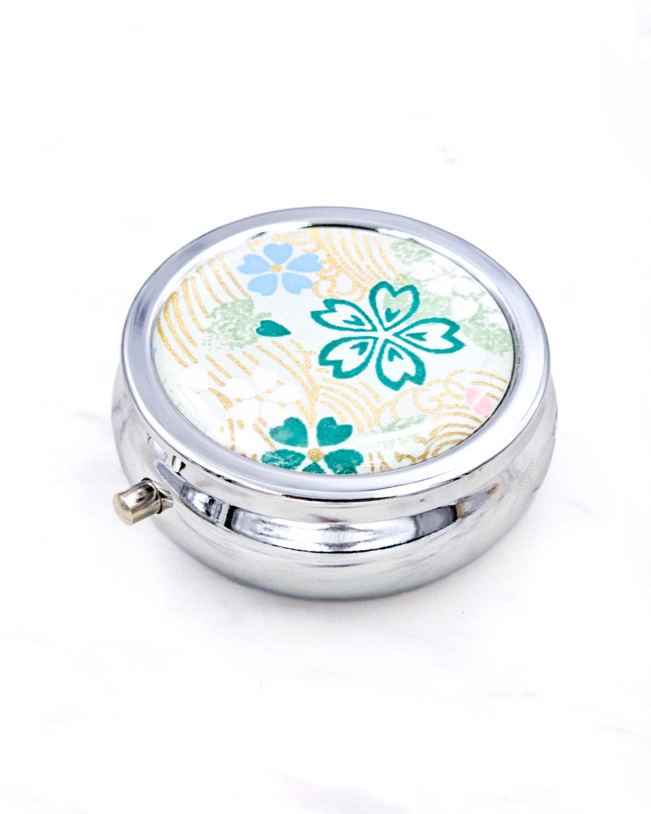 Silver metal pill box featuring green, white, and blue cherry blossoms on green background with metallic gold accents.