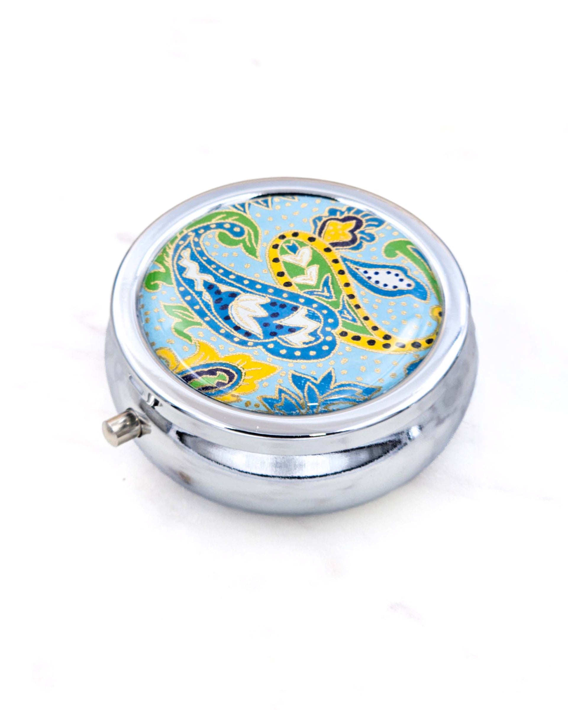 Silver metal pill box featuring a green and yellow paisley design on a light blue background with metallic gold accents.